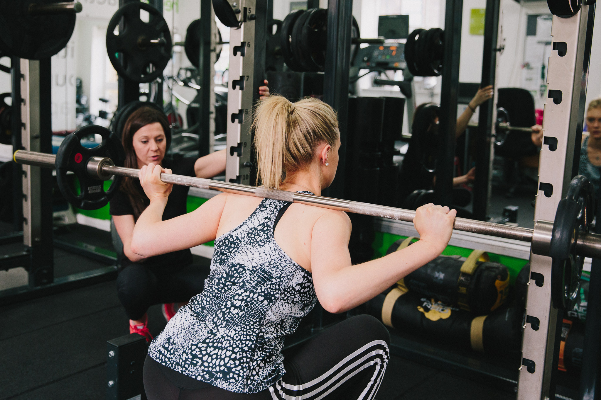 female client barbell squatting coached by personal trainer